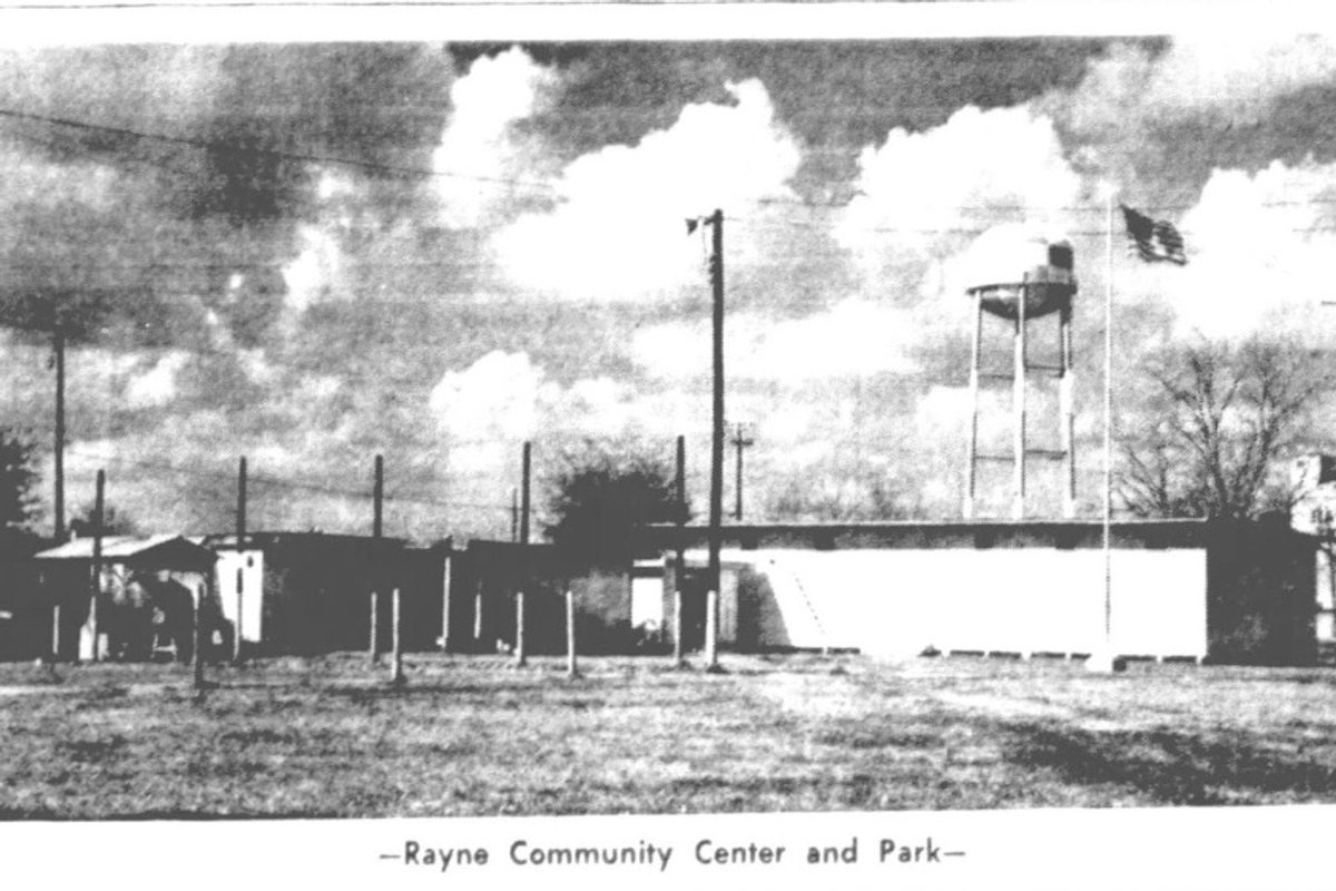 Historic black-and-white photograph of the Rayne Community Center and Park with the city water tower and American flag.